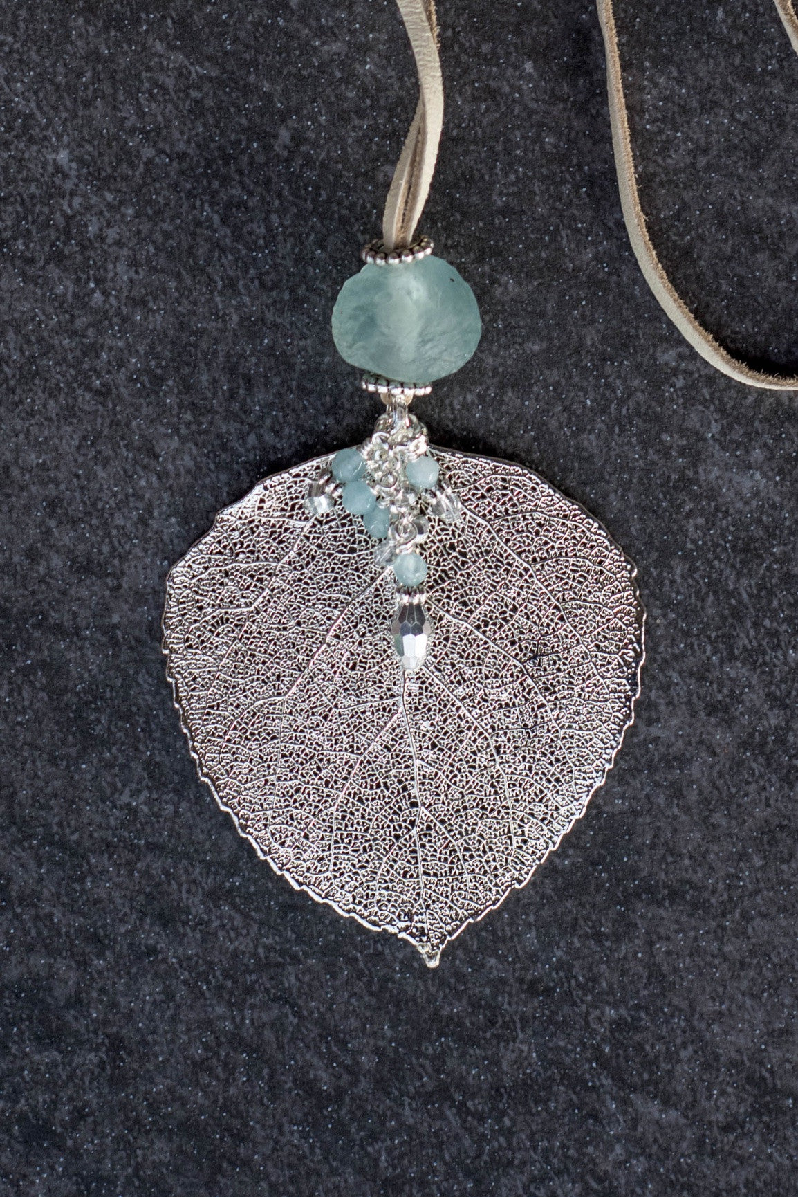 Single re-cycled African glass bead with a large silver Aspen leaf finished with a stunning crystal dangle .  Deerskin leather